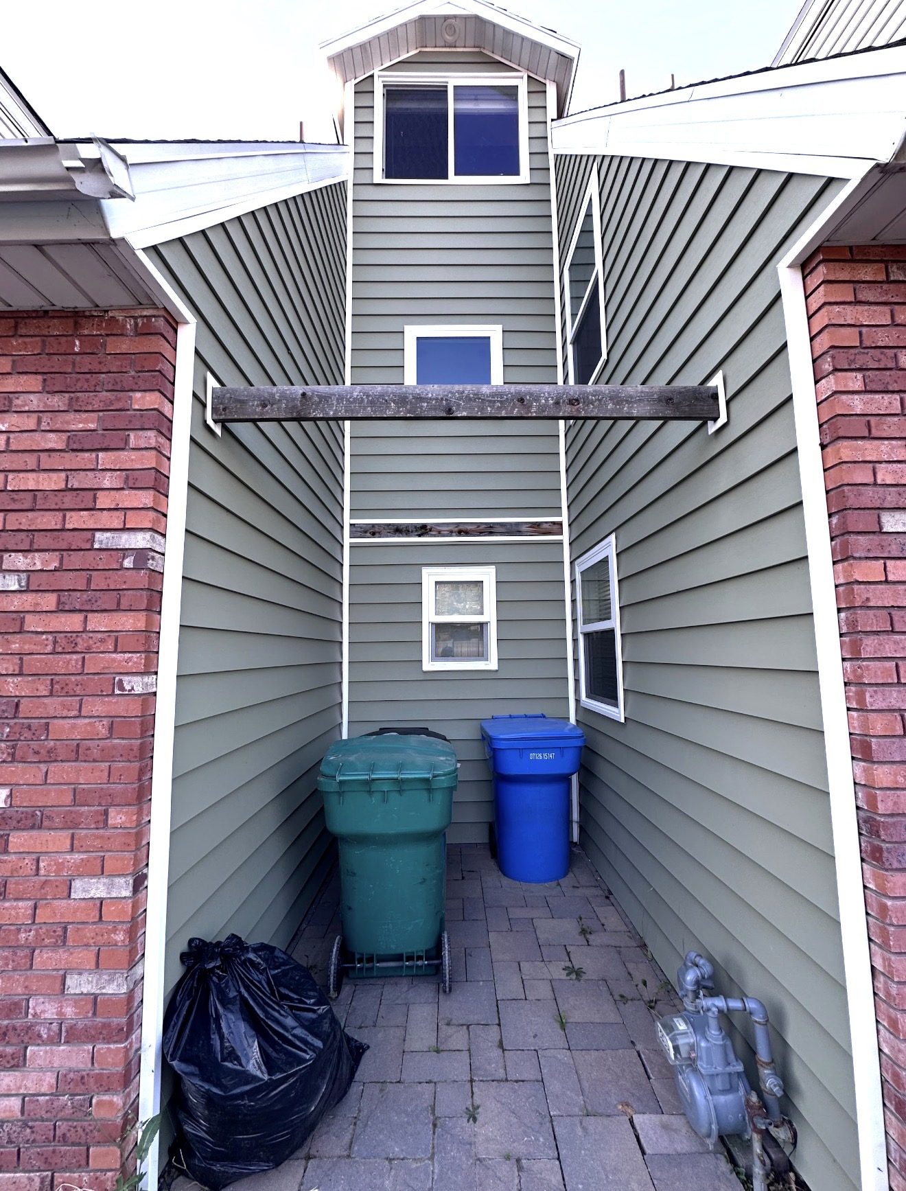 Middle nook before, green vinyl siding between two brick wings