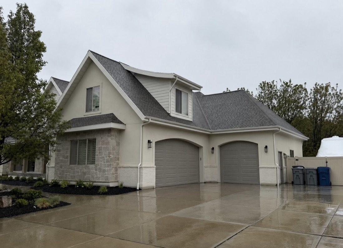 Home after, white skim-coated stucco with painted grey garage doors