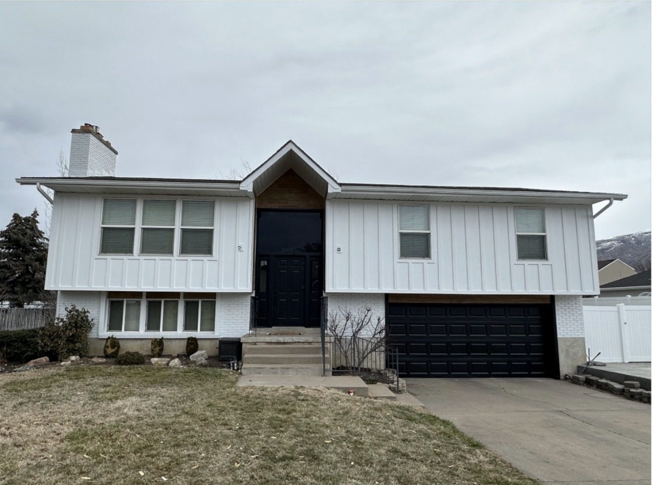 Split-level home after, white James Hardie board and batten siding with black door and garage